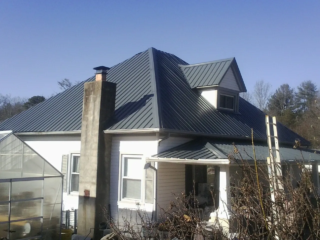 Dark blue standing seam metal roof on a white farmhouse with dormer — Slate & Tile Roof Repair by Roofing Brothers in Eskridge