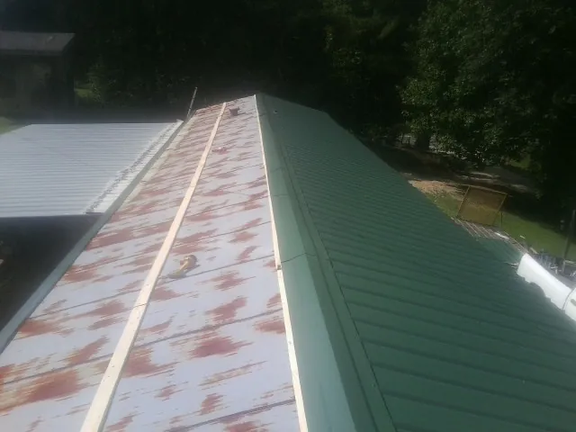 Old rusted panels beside newly installed green metal roofing — Wind Damage Roof Repair by Roofing Brothers in Eskridge