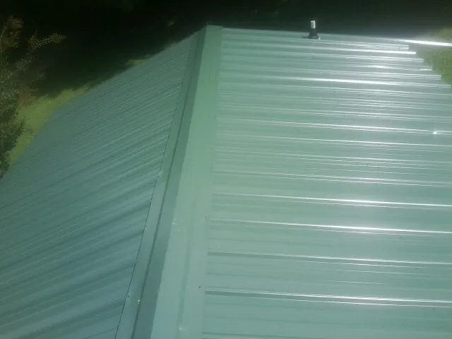 New green metal panels meeting at the ridge of a roof — Flat Roof Repair work by our crew in Eskridge