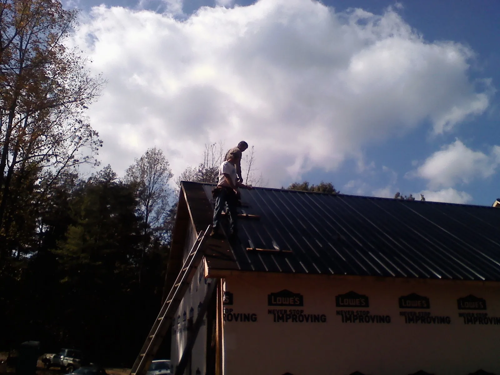 Roofer fastening dark metal panels high against a cloudy sky, from a Roof Inspection job in Eskridge
