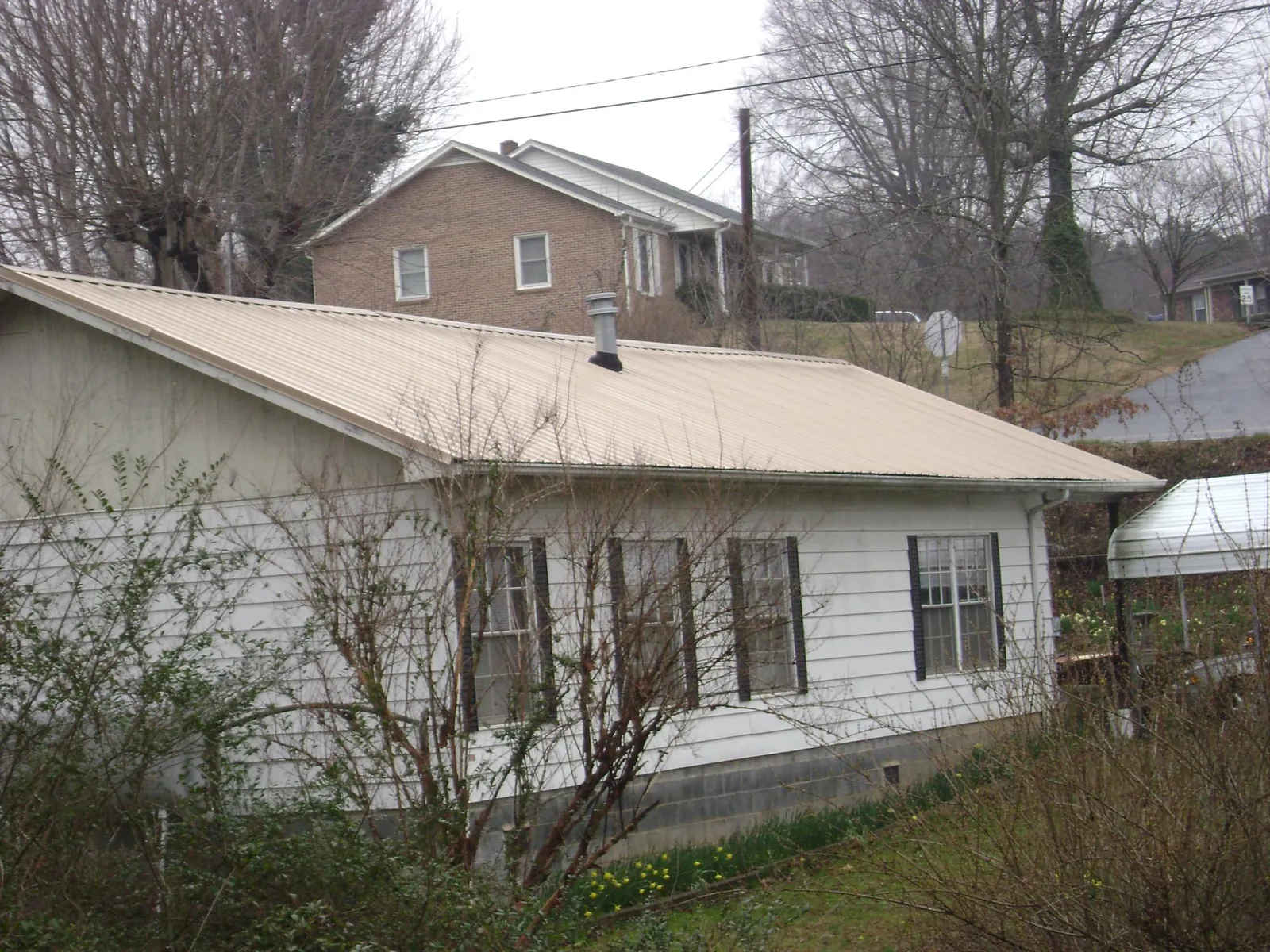 Tan metal roof on a white sided house set into a hillside — Commercial Roofing by Roofing Brothers in Eskridge